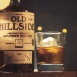 Jesse Carpenter, co-founder of Old Hillside Bourbon, stands holding a bottle of the Durham-inspired bourbon brand he launched with fellow Hillside High School alumni.